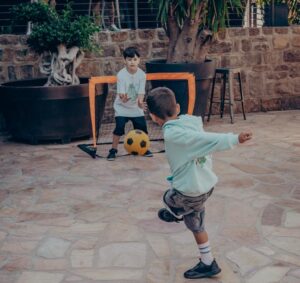Zwei Kinder spielen im Garten mit einem Fußball und Hockeyschlägern.