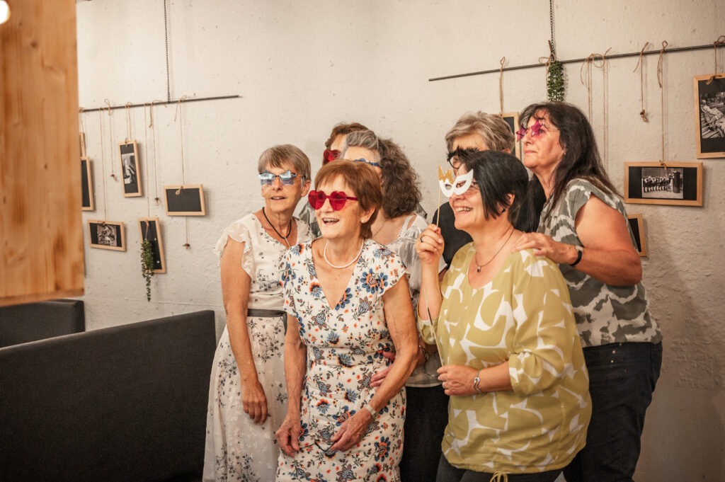 Gruppe älterer Frauen in einer Galerie, einige tragen Brillen, lachen und schauen nach vorne.