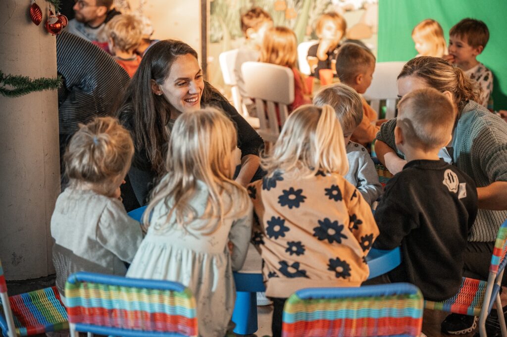 Eine Gruppe von Kindern und einer erwachsenen Frau sitzen um einen Tisch und unterhalten sich.