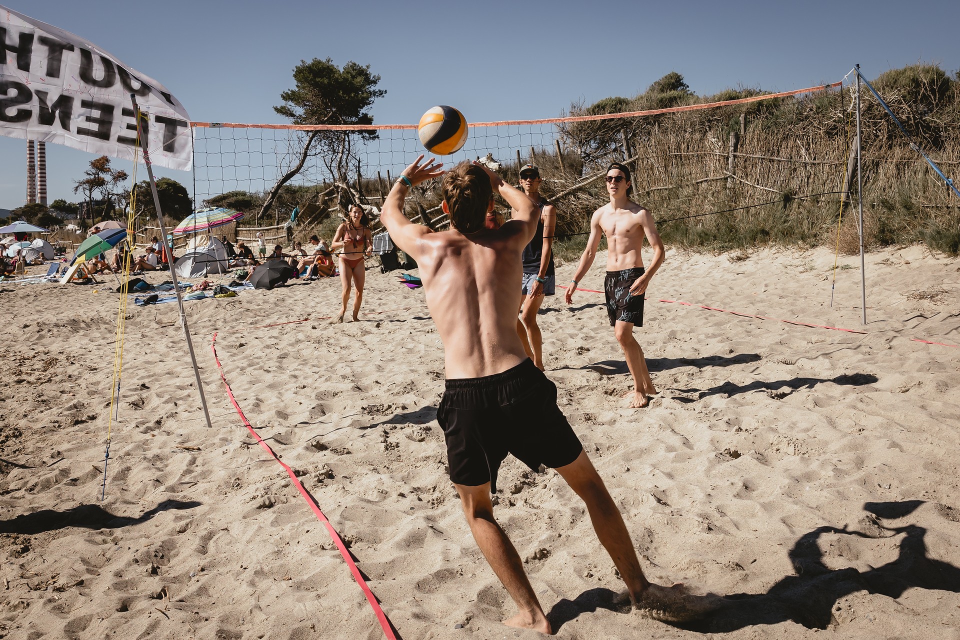 Ein Mann springt hoch, um den Volleyball zu schlagen, während andere am Strand zuschauen.