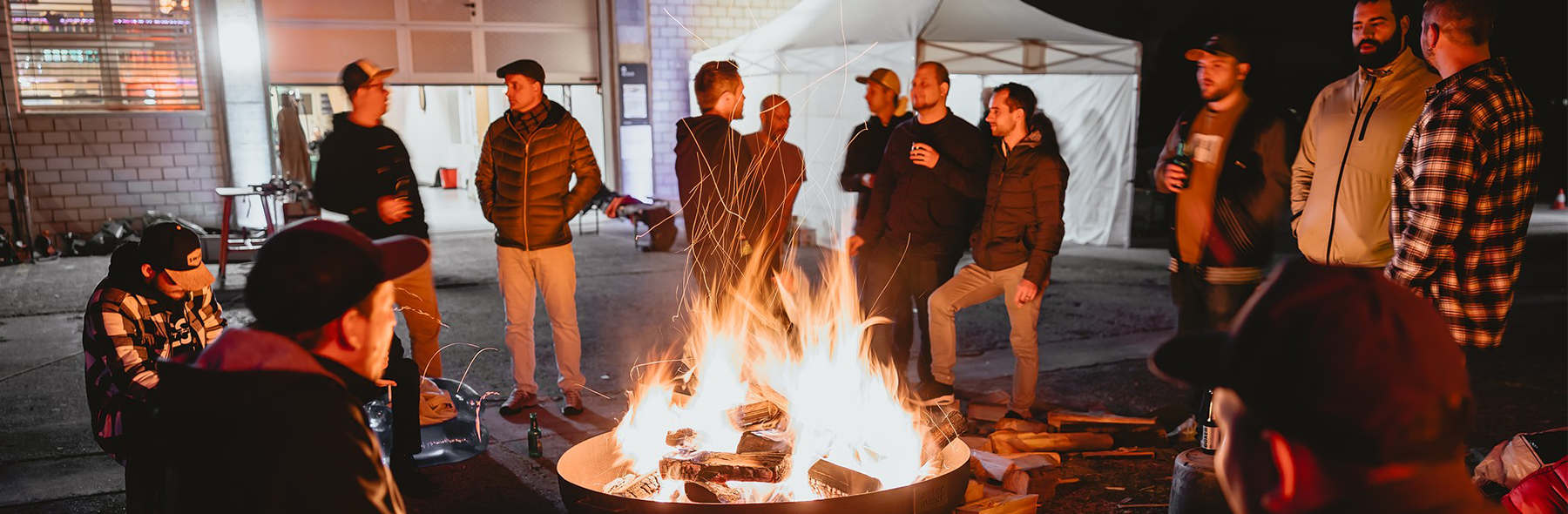 Menschen sitzen und stehen um eine Feuerstelle im Freien.