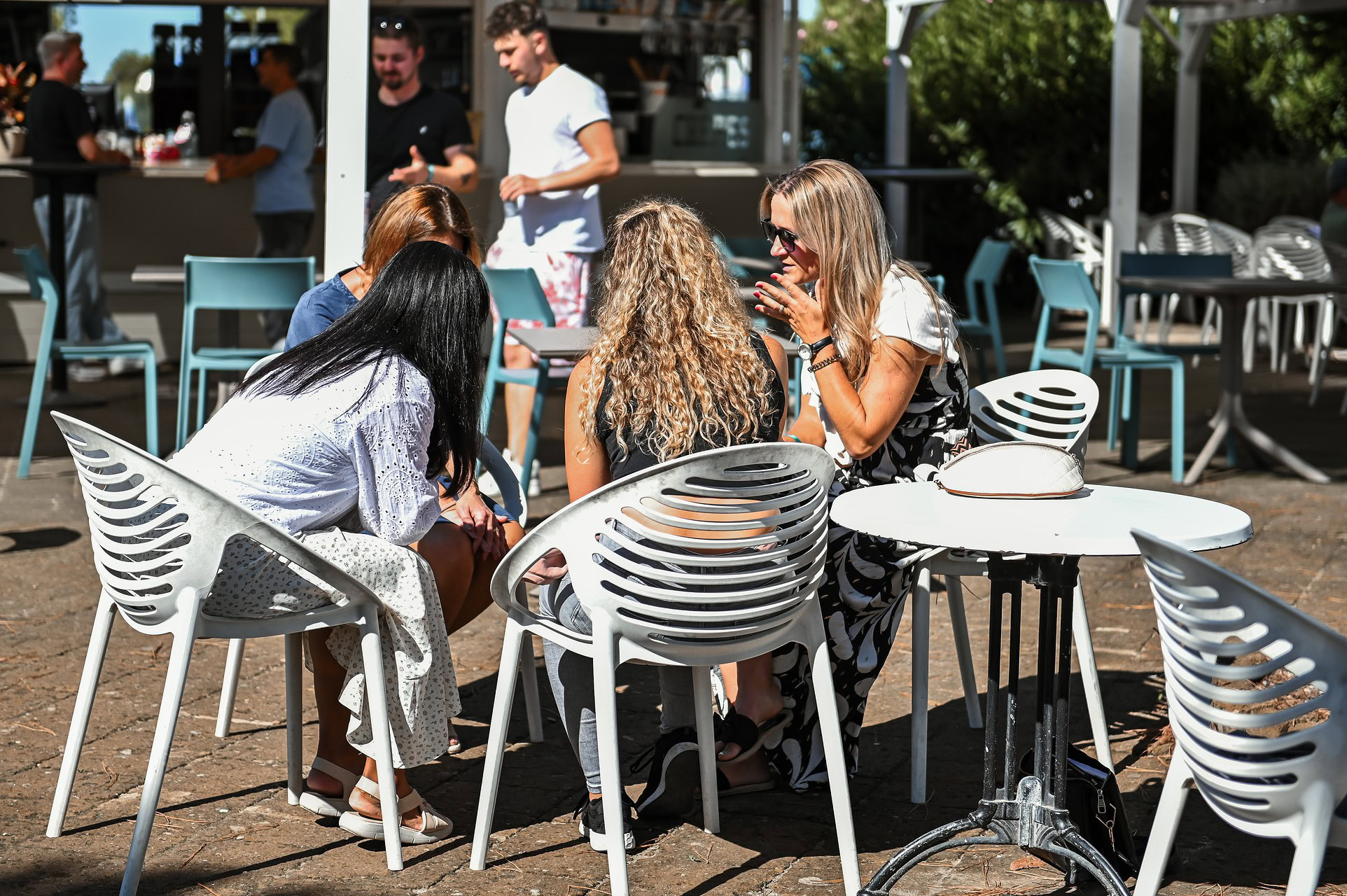 Vier Frauen sitzen an einem runden Tisch im Freien, unterhalten sich.