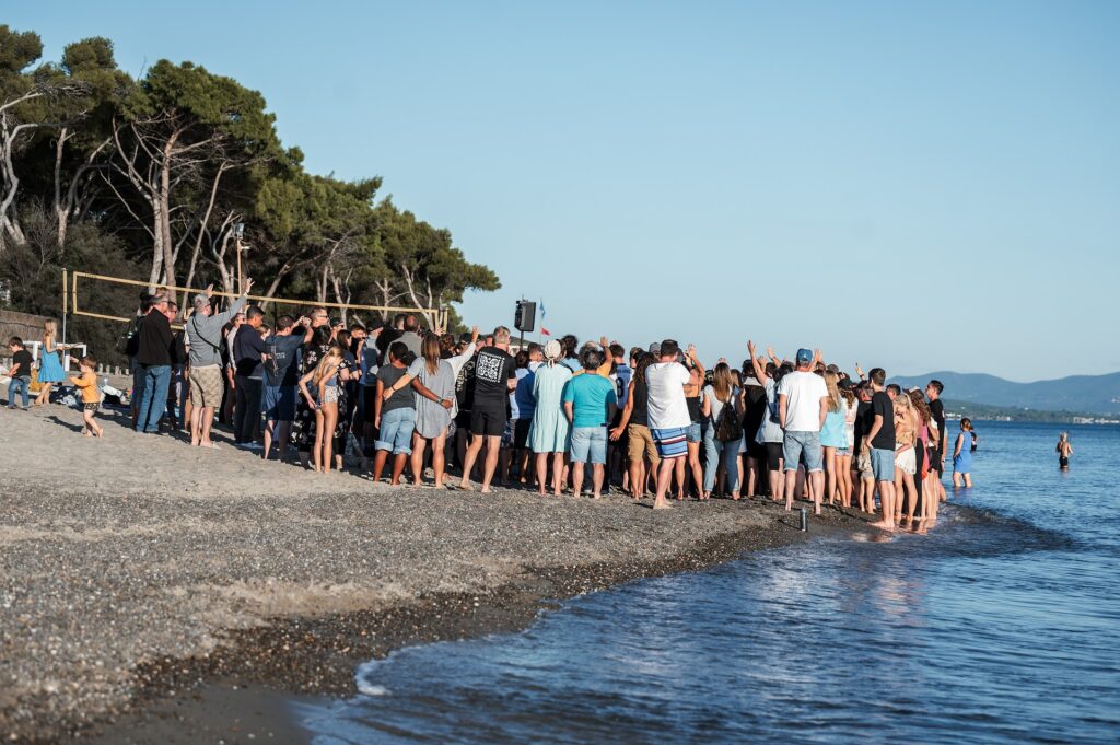 Menschenmenge versammelt sich am Strand, einige schauen aufs Wasser.