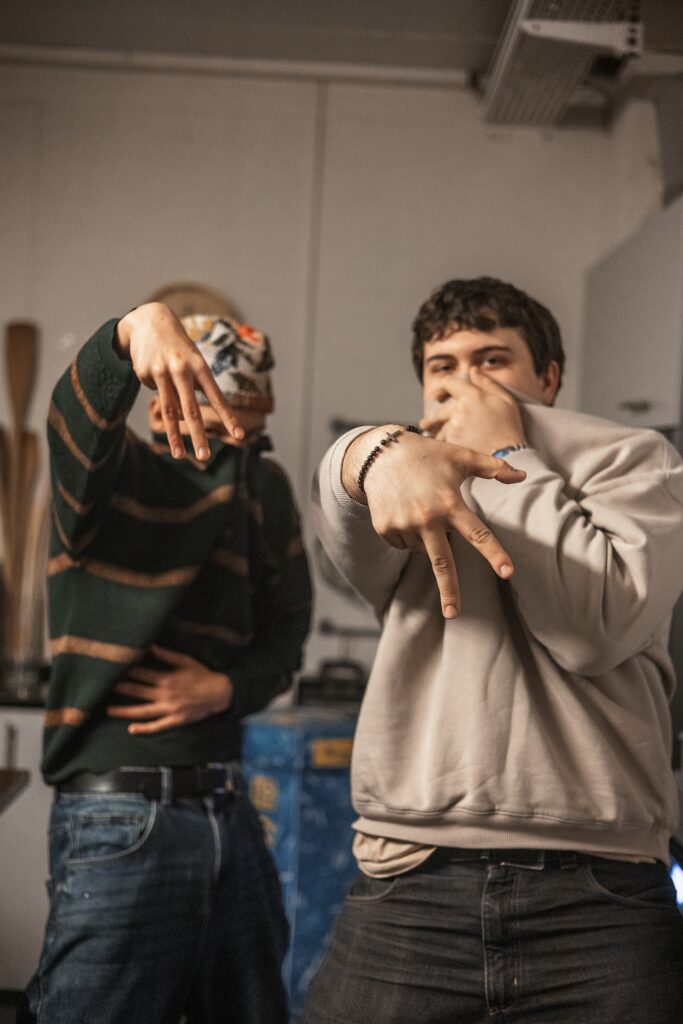 Zwei Jugendliche zeigen Handzeichen, einer trägt einen Pullover, der andere eine Jacke.