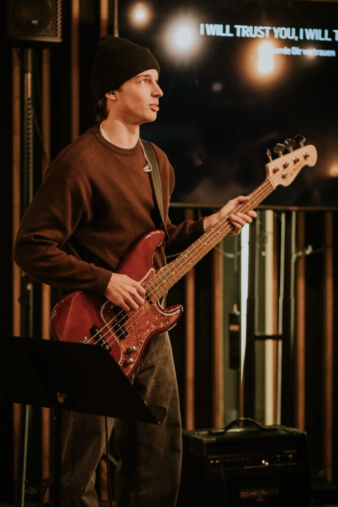 Frau mit schwarzem Hut und braunem Pullover spielt E-Gitarre auf Bühne.