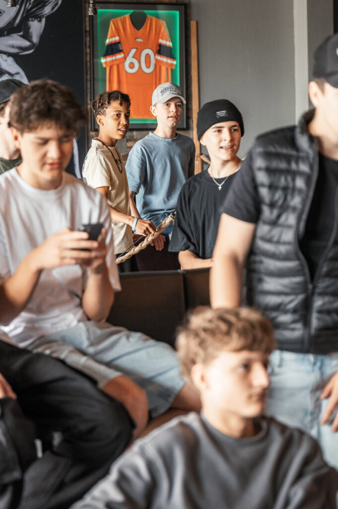 Junge Menschen sitzen und stehen in einem Raum, einige schauen auf ihr Smartphone.
