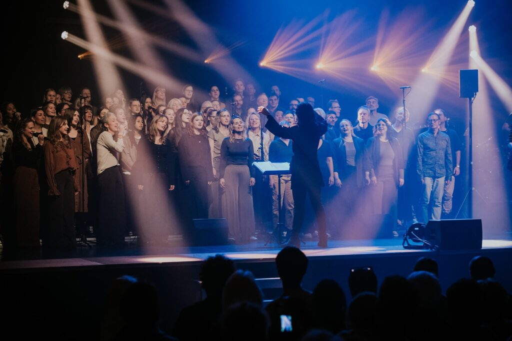 Chor auf Bühne bei einem Konzert, dirigiert von einer Person.
