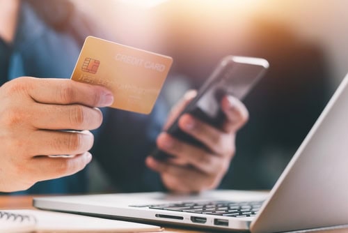 Person mit Kreditkarte und Smartphone beim Online-Shoppen, DA, Nahaufnahme, moderne Einkaufs- und Finanztechnologie, digitales Bezahlen, München, Kreditkarte, Laptop, Alltag, Technik, Innovation.