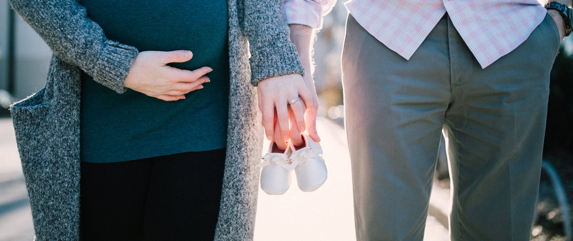Zwei Erwachsene halten die Hände eines Babys, das weiße Schuhe trägt.