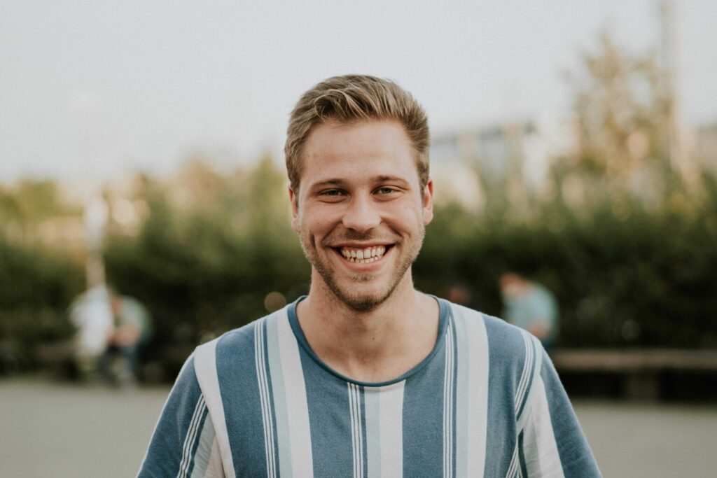 Ein junger Mann mit kurzen, hellbraunen Haaren und einem breiten Lächeln.