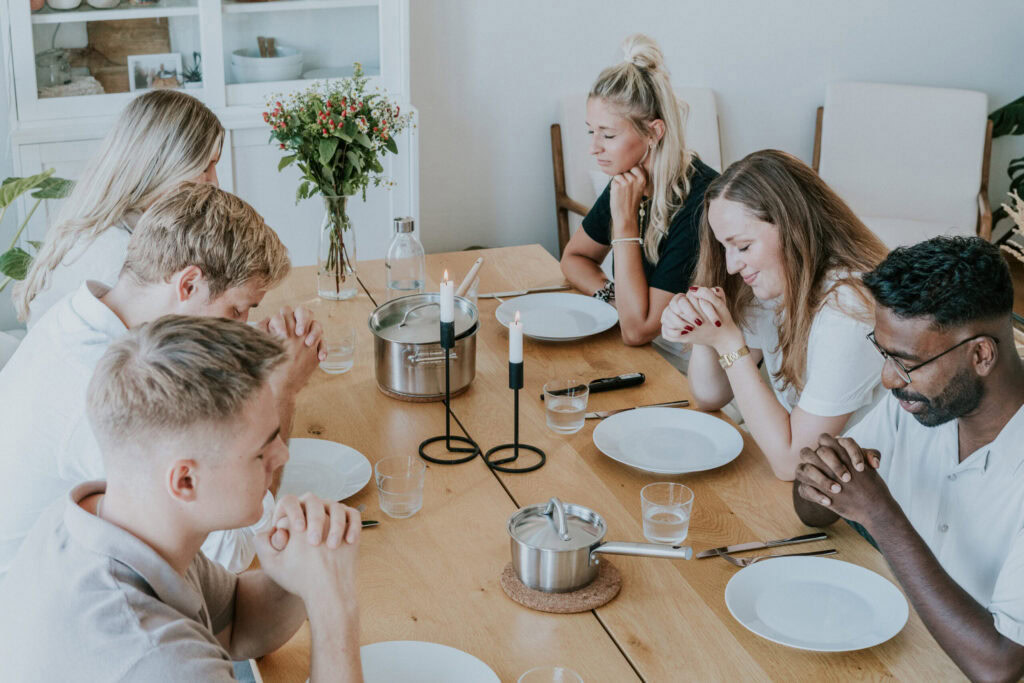 Familie mit sechs Personen sitzt beim Essen an einem Holztisch.
