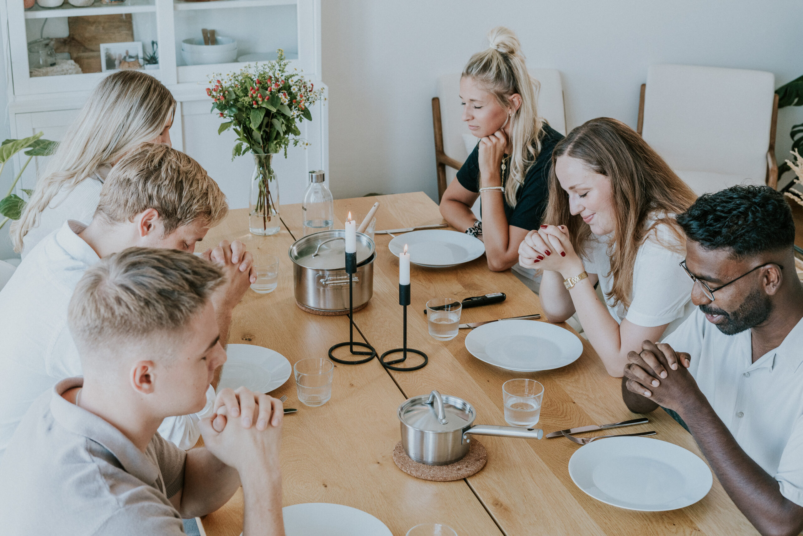 Familie mit sechs Personen sitzt beim Essen an einem Holztisch.