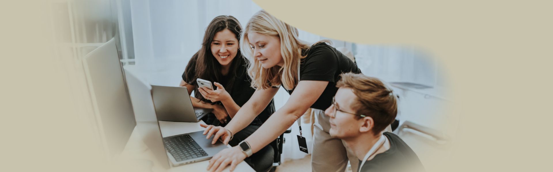 Drei junge Menschen arbeiten gemeinsam an einem Tisch mit Laptops und Smartphone.