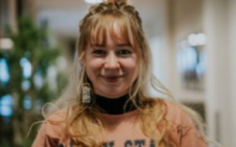 Ein junges Mädchen mit blonden Haaren, das in einem Innenraum lächelt.