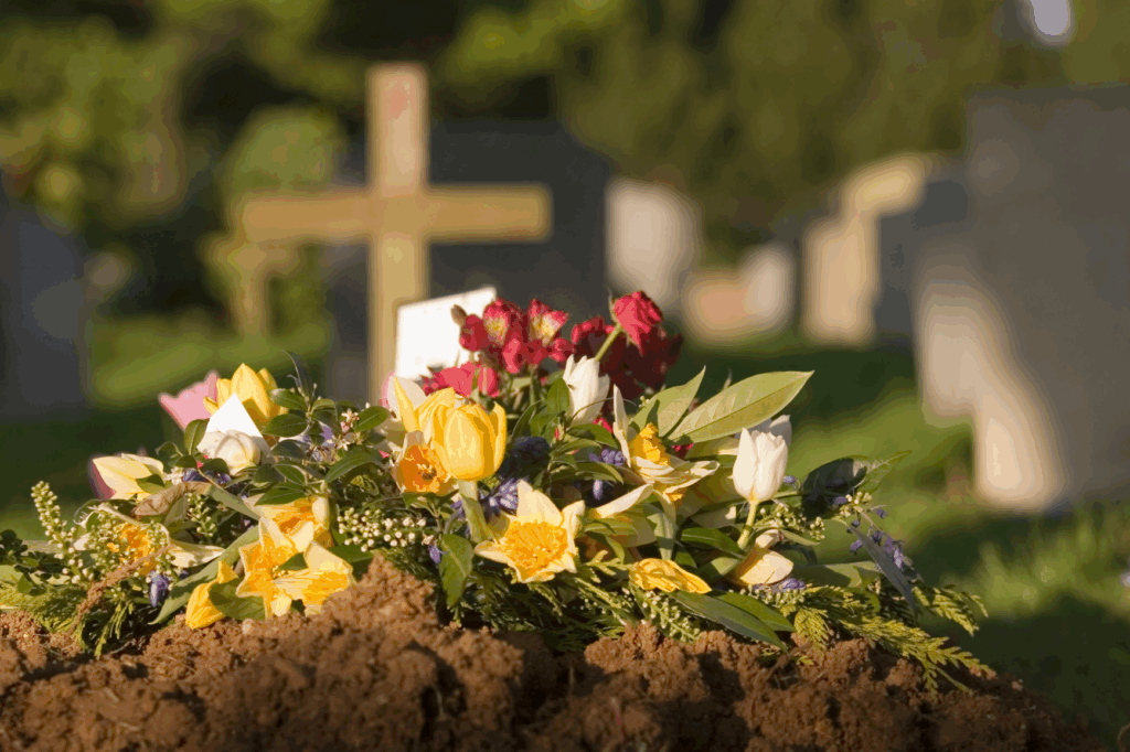 Blumen liegen auf Erde vor einem Grabstein im Friedhof.