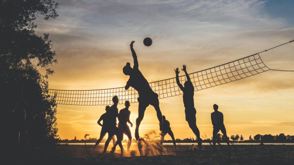 Silhouetten von Menschen, die Volleyball am Strand bei Sonnenuntergang spielen.