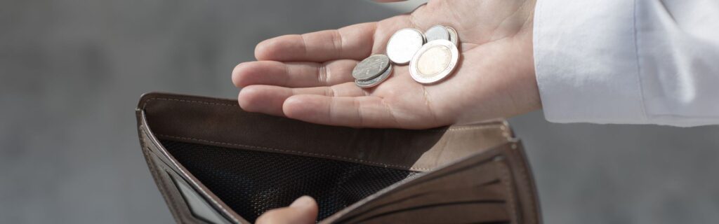 Hand holding coins and banknotes, wallet visible in the background.