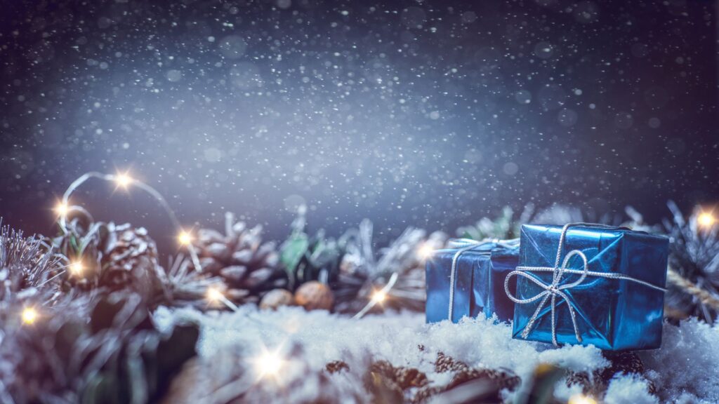 Blaue Geschenkbox mit silberner Schleife im Schnee bei Schneefall.