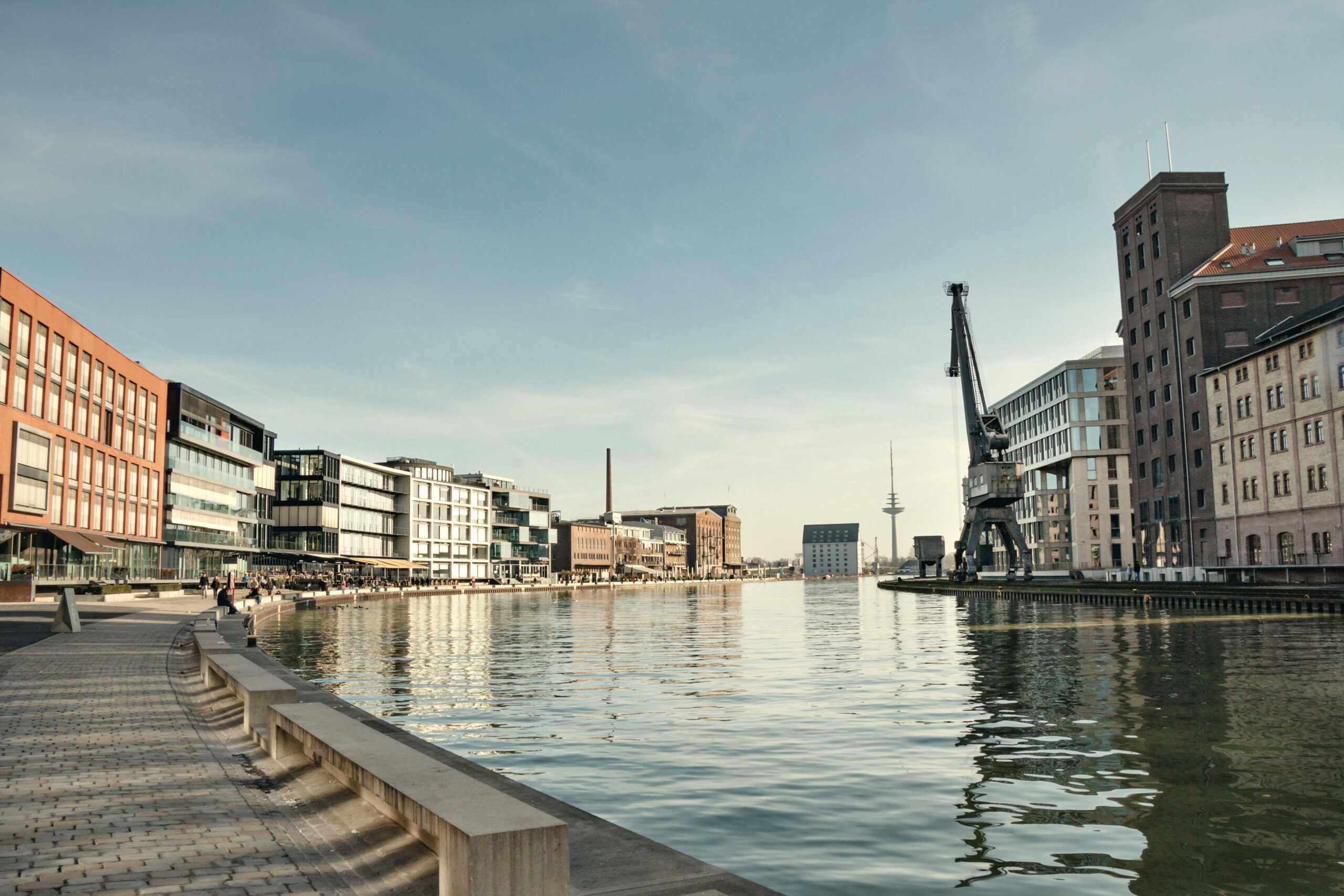 Ein Blick auf den Hafen mit Wasser, modernen Gebäuden und einem Kran im Hintergrund.