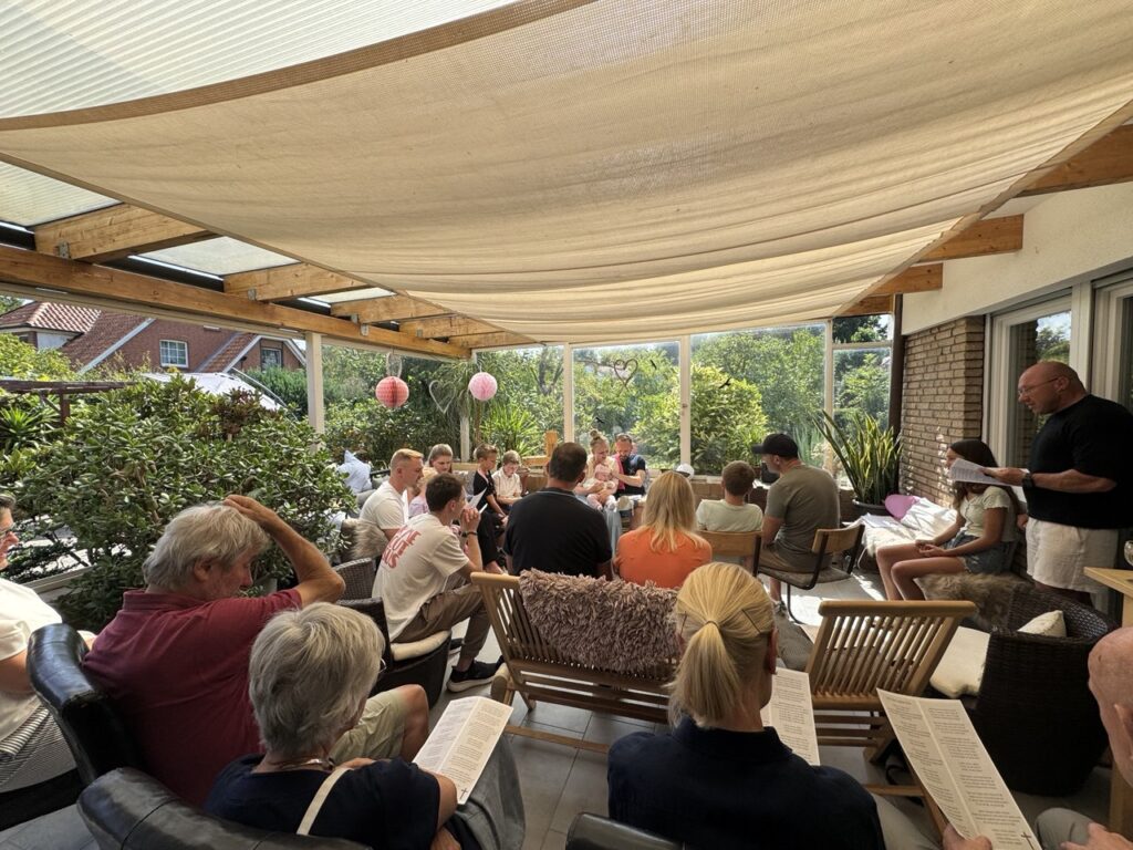 Gruppe von Menschen liest gemeinsam auf einer Terrasse mit Sonnenschutz.
