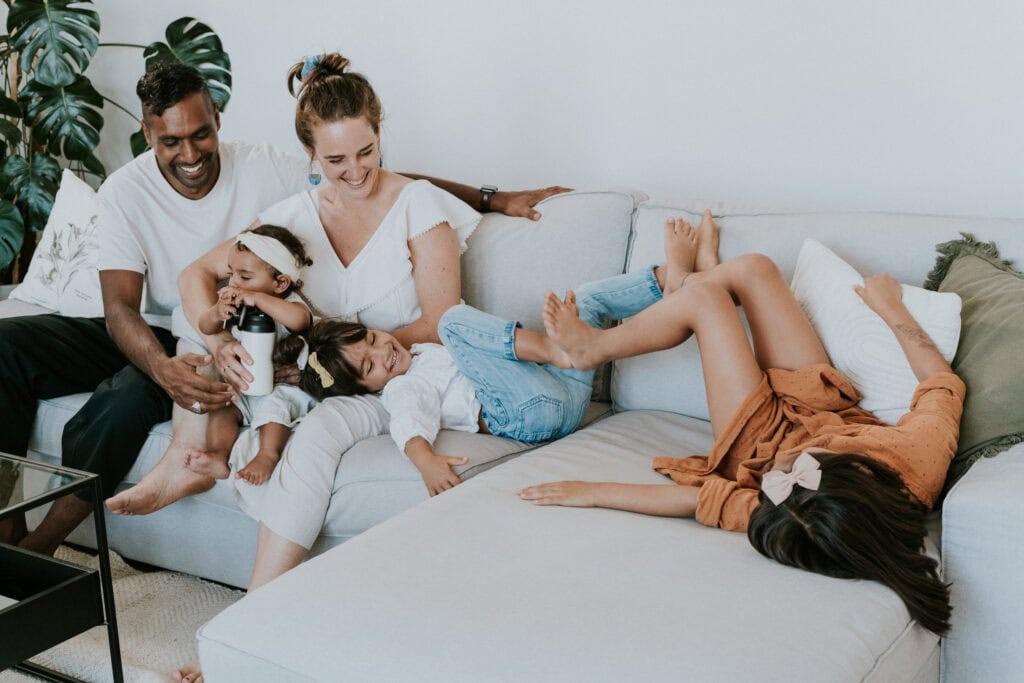 Fröhliche Familie beim gemeinsamen Spielen auf dem Sofa, symbolisiert Familienzusammenhalt, Glück und Harmonie, perfekt für Keywords wie Familienzeit, Zusammenhalt, Eltern-Kind-Beziehung, Familienleben.