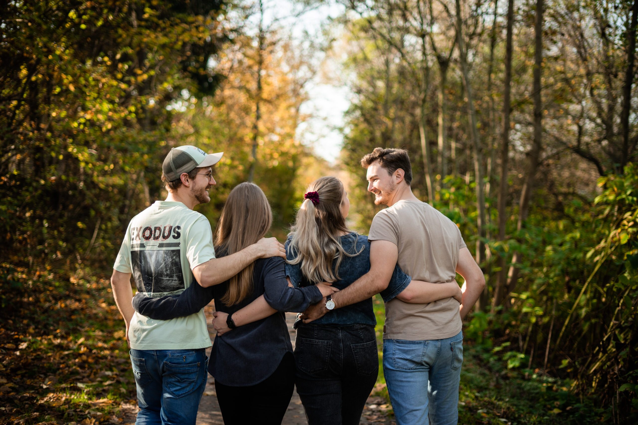 Gruppe junger Menschen, die im Wald spazieren gehen und sich umarmen, symbolisiert Gemeinschaft und Freundschaft in einem natürlichen Umfeld.