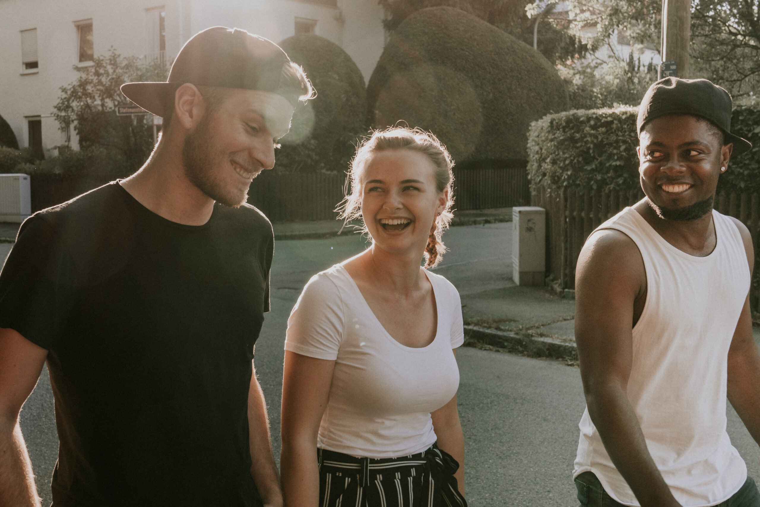 Drei junge Menschen gehen im Sonnenlicht auf der Straße spazieren, lachen und unterhalten sich.