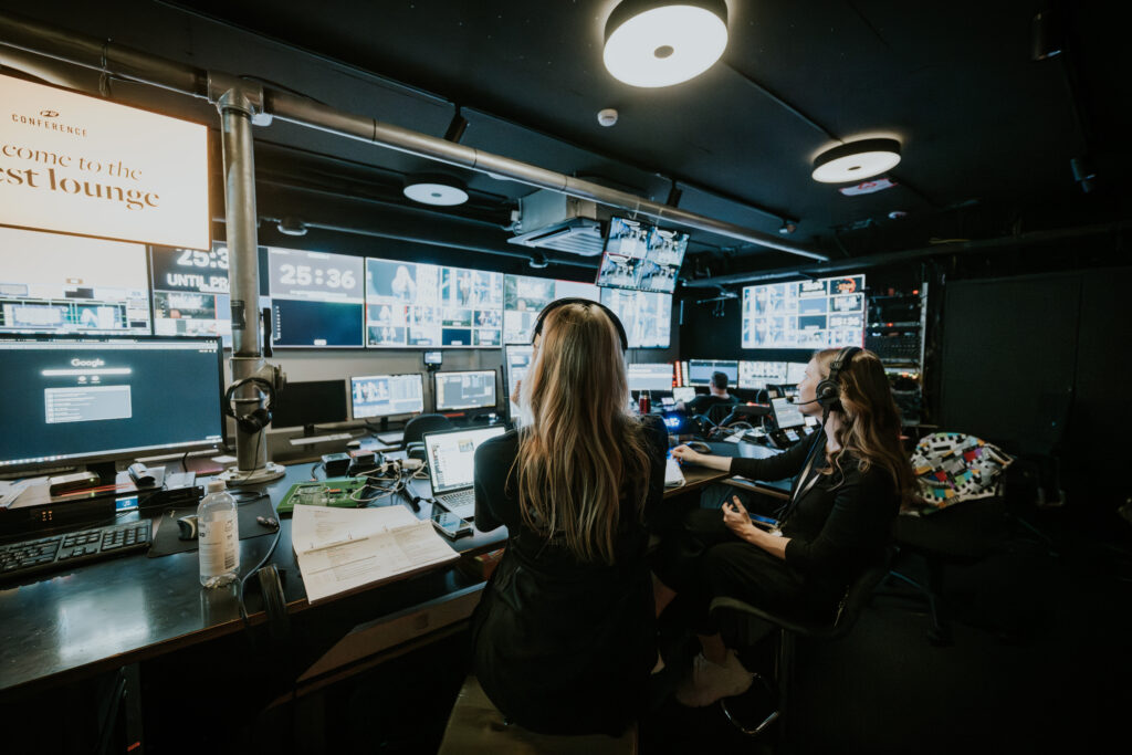 Two women working at a control room with multiple screens displaying data and video feeds.