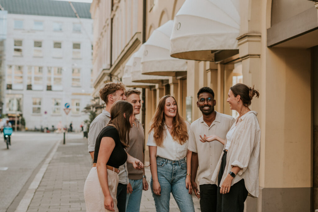 Six young adults standing outside on a city street, talking and smiling.