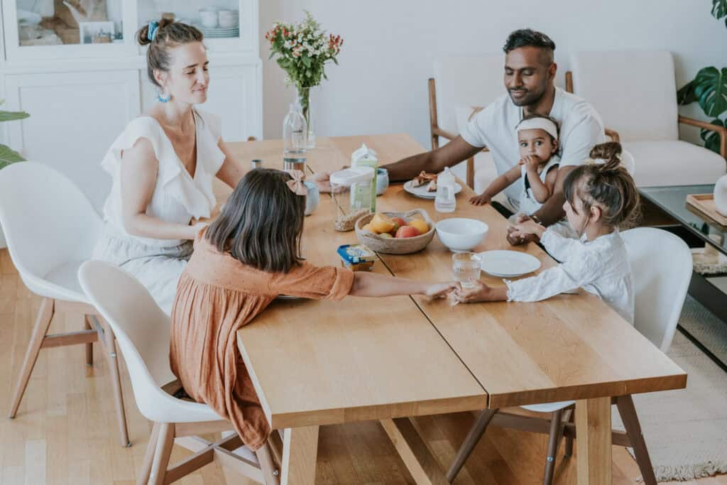 A family of six sitting around a wooden dining table with food and drinks.