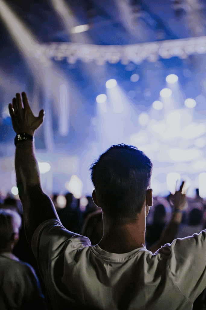 A person with short hair and a white shirt raising their hand in front of a stage with blue and whit.