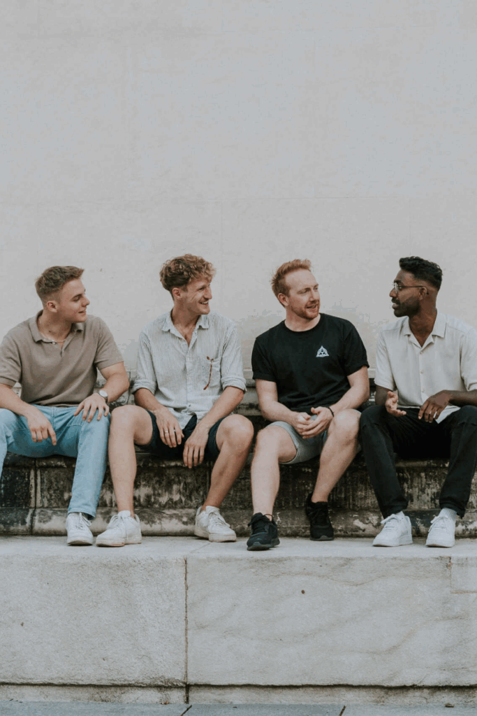 Four young men sitting on a stone wall, engaged in conversation.