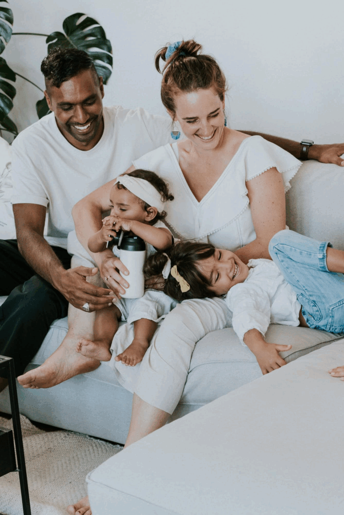 Three people, two children and an adult woman, sitting on a light-colored sofa. The woman and a man.