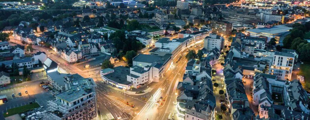 Moderne und historische Gebäude in Rhein-Main bei Dämmerung, beleuchtet mit Straßenzügen, Geschäften und Wohnhäusern, die den urbanen Charakter der Region zeigen.