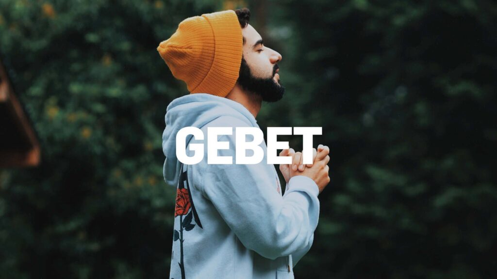 Ein junger Mann betet in einem Wald, trägt eine gelbe Mütze und eine graue Jacke, symbolisiert spirituelle Verbundenheit und Gebet im Freien.