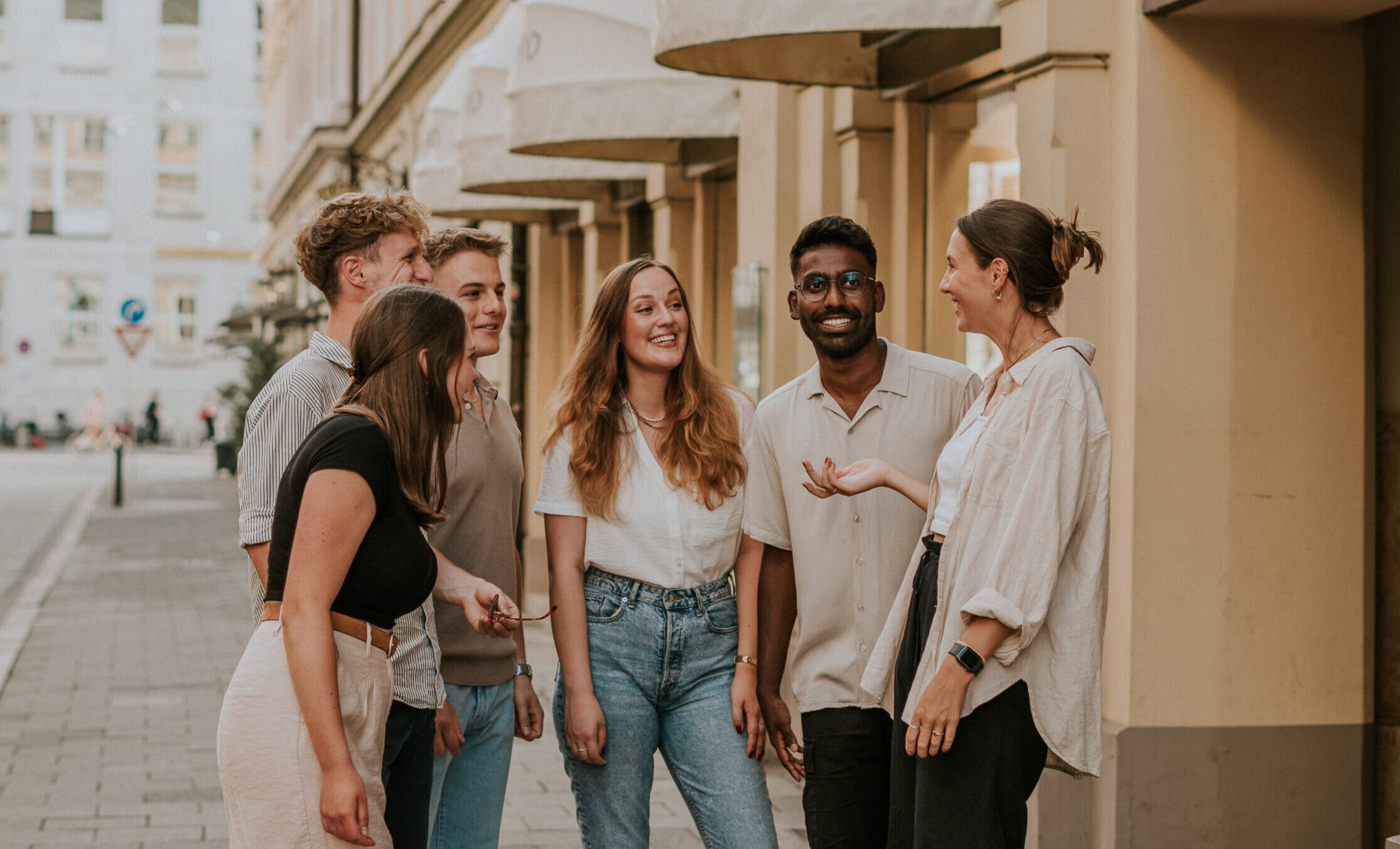 Vielfältige Gruppe junger Menschen im Gespräch vor einem stilvollen Stadthaus, urbaner Treffpunkt für Community und soziale Interaktion, inklusive freundlichem Austausch und gemeinsamer Zeit, symbolisiert Gemeinschaft und Vernetzung in der Stadt, modern urbane Atmosphäre, kulturelle Vielfalt.