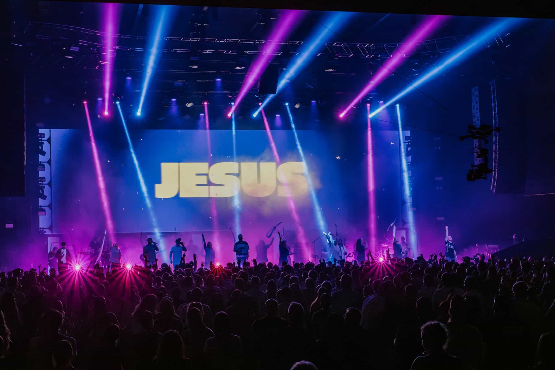 Bühne mit "JESUS" Schrift, Lichter und Menschenmenge.