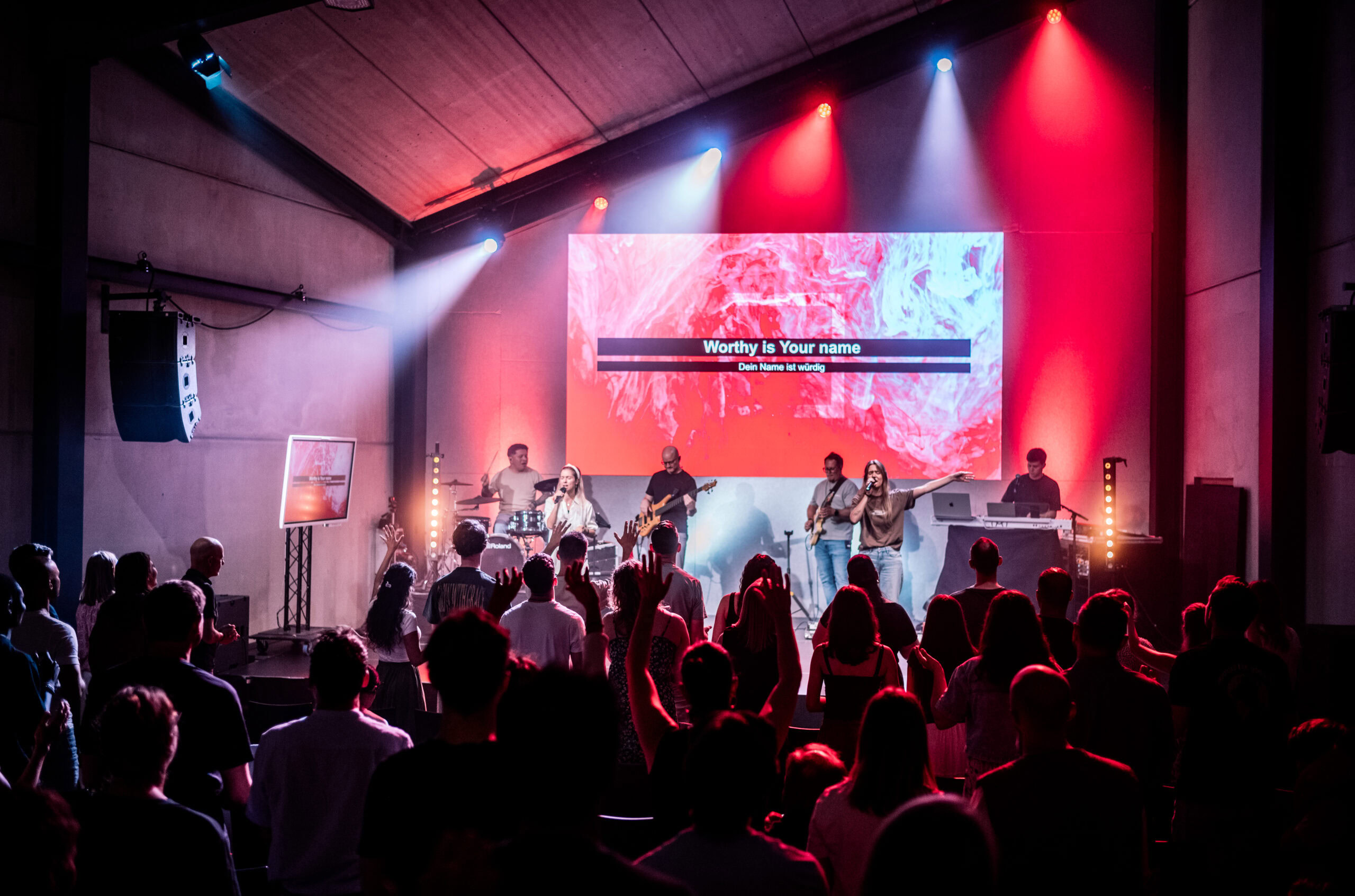 Menschen auf einer Bühne bei einem Konzert, mit bunten Lichtern im Hintergrund.