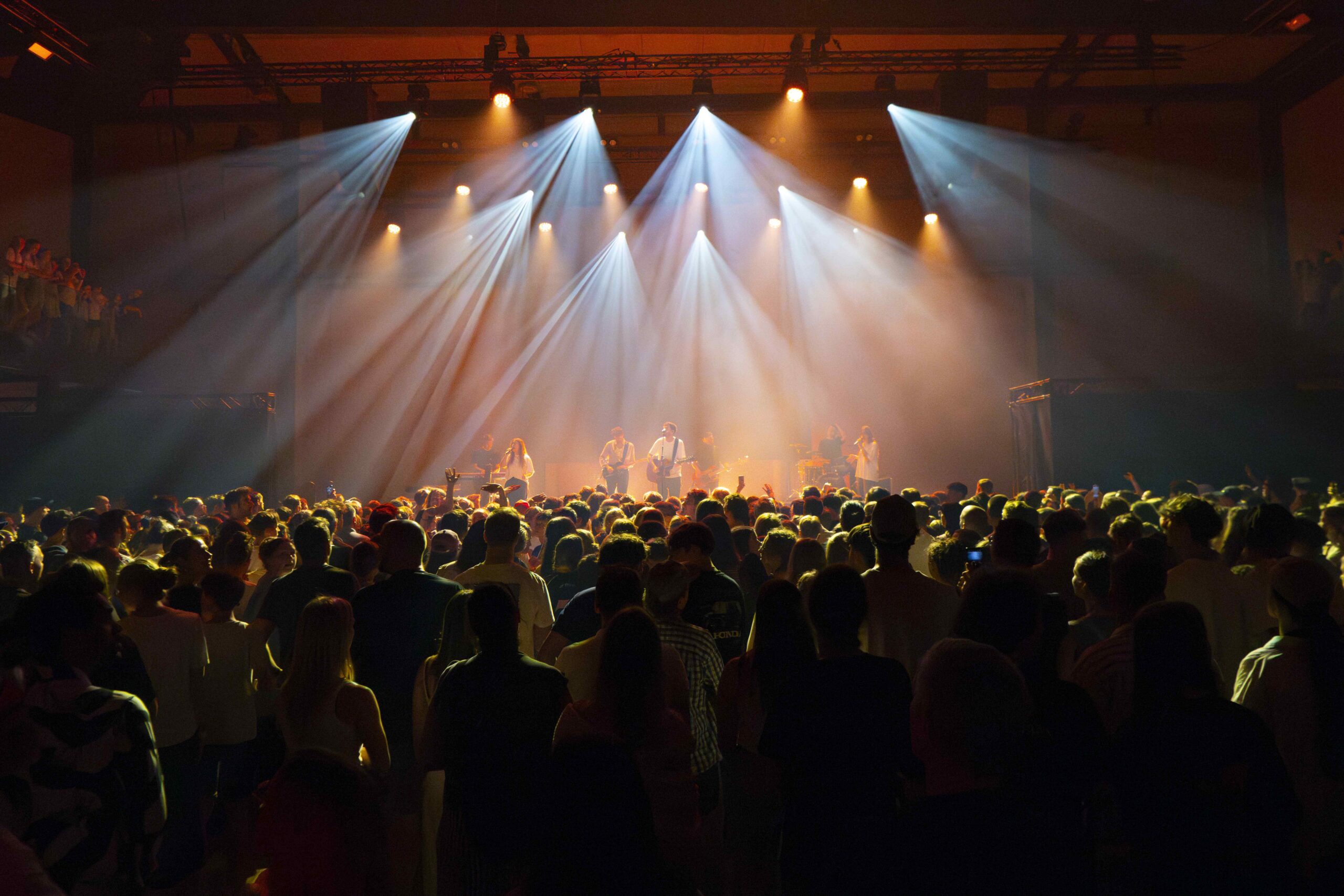Menschenmenge vor einer Bühne mit Scheinwerfern, Konzert oder Veranstaltung.