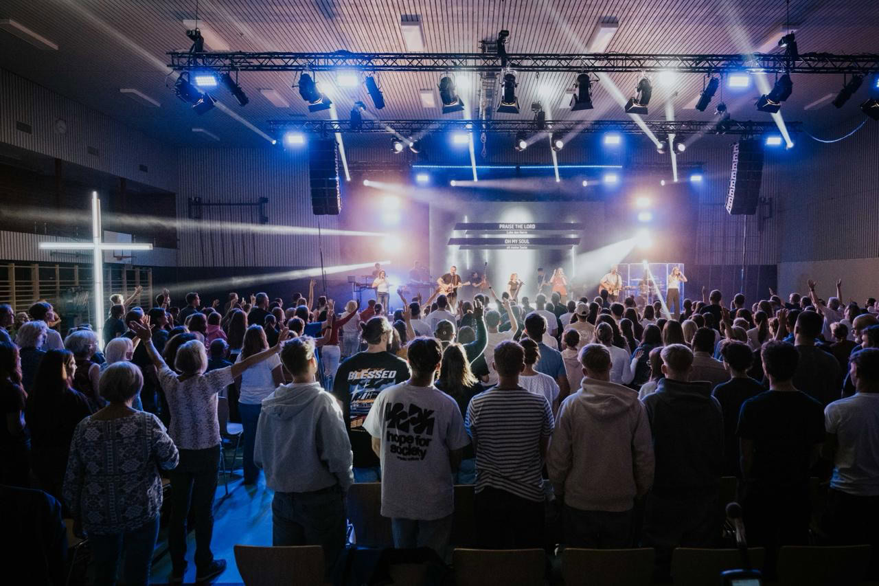 Ein Publikum steht vor einer Bühne mit Lichteffekten und Musik.