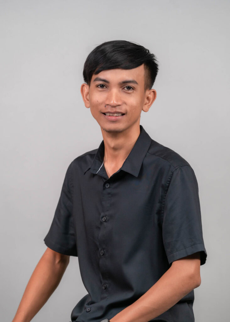 Junges asiatisches Kirchenmitglied in Siem Reap, Kambodscha, lächelnd, trägt dunkle Hemd, steht vor neutralem Hintergrund.
