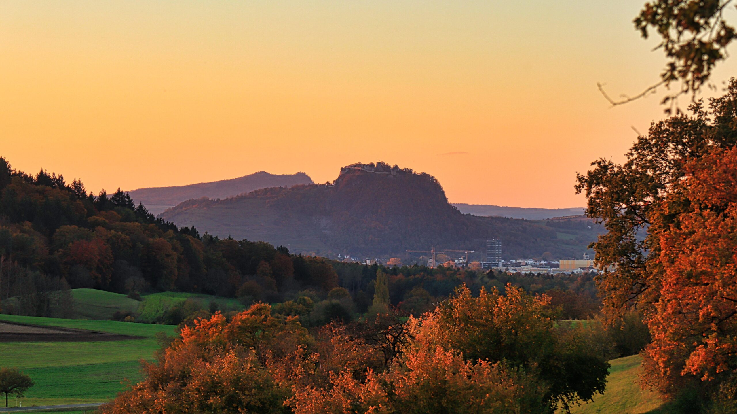 Berglandschaft mit Sonnenuntergang im Hintergrund und buntem Herbstlaub im Vordergrund.