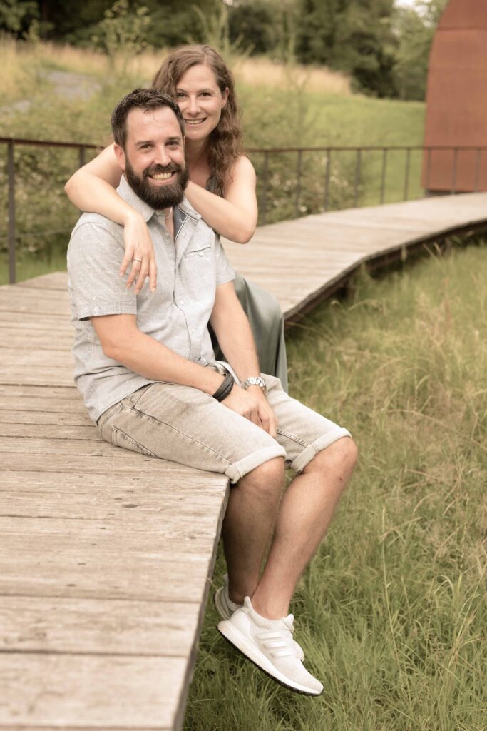 Ein Mann sitzt auf einer Holzbrücke, eine Frau umarmt ihn von hinten.
