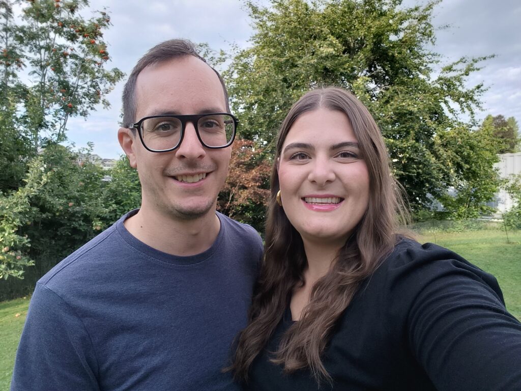 Ein Mann und eine Frau stehen im Freien vor Bäumen und grünem Gras.