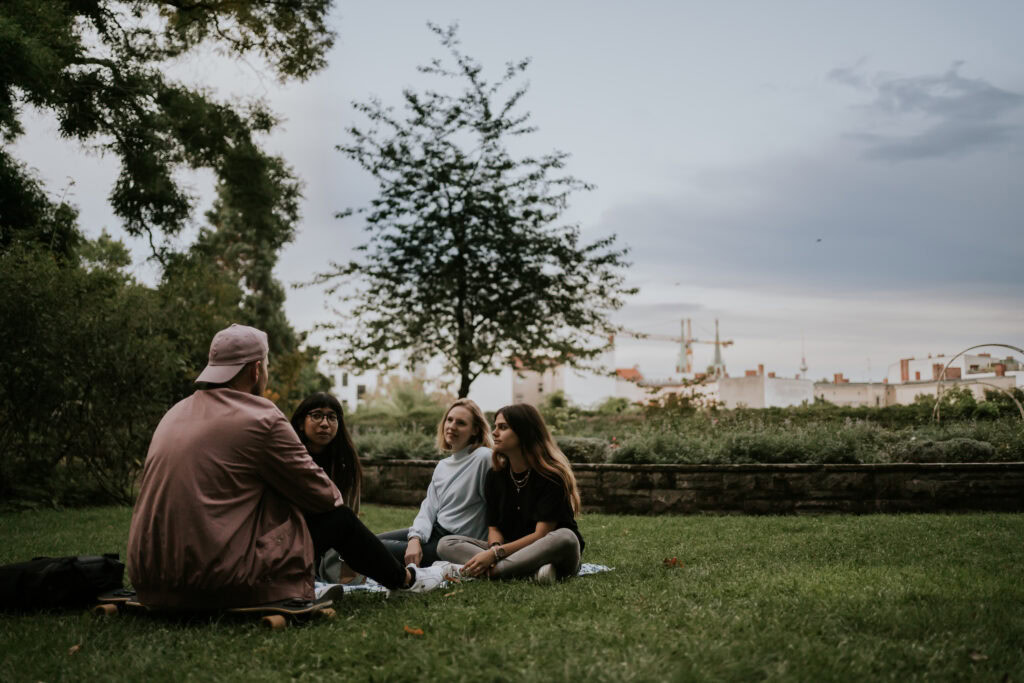 Freunde im Park beim Gespräch, Natur, Entspannung, Gemeinschaft, jugendliche, Freizeit, urbanes Umfeld, Abendstimmung, gesellschaftliche Aktivitäten, soft focus, lifestyle, outdoor, junge Leute, urbane Atmosphäre.