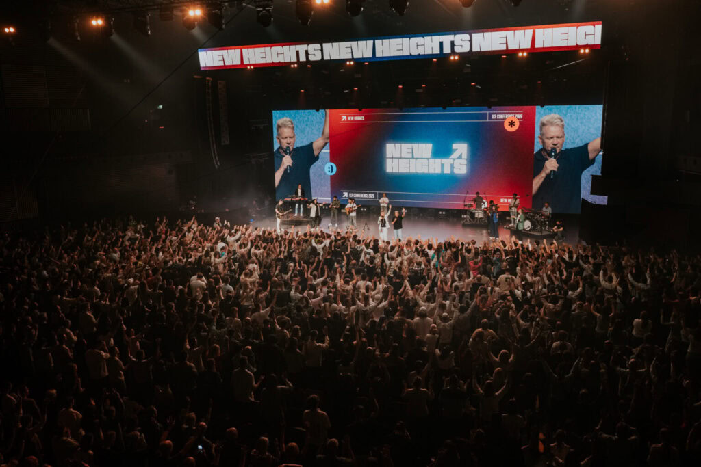Große Bühne mit Sänger und Band, Publikum im Saal, große Bildschirme.