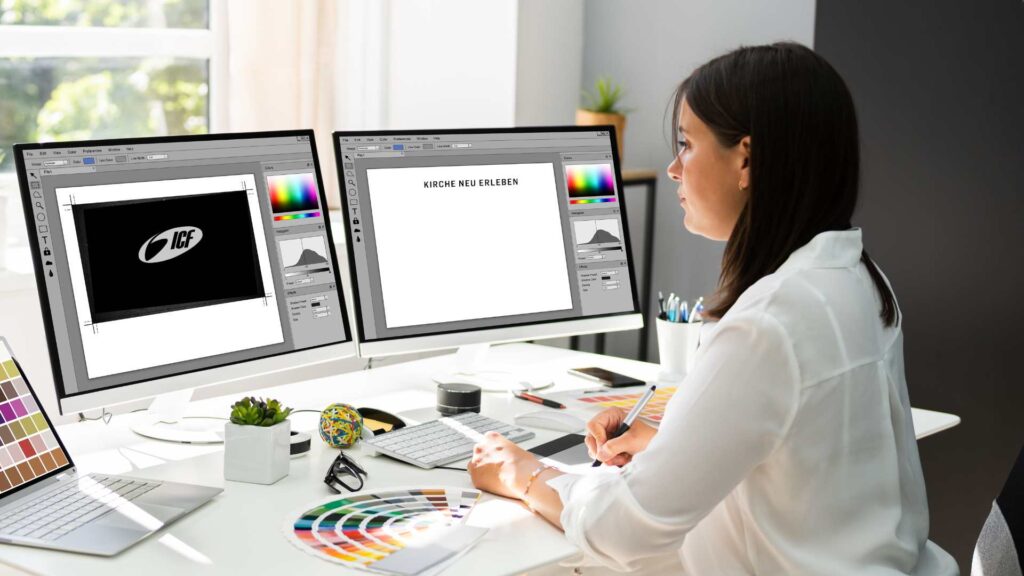 Frau arbeitet an einem Grafikdesign-Projekt auf zwei Computerbildschirmen, umgeben von Farbpaletten und Design-Tools, in einem modernen Büro.