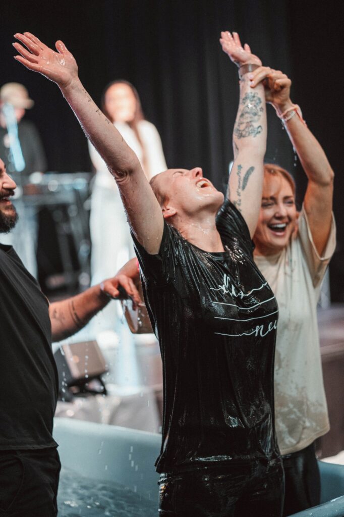 Menschen bei einer religiösen Zeremonie mit erhobenen Armen, Freude und Gemeinschaft, im Hintergrund Musiker und dunkler Vorhang, symbolisiert spirituelle Erfahrung und Zusammenhalt.