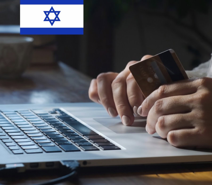 יד מחזיקה כרטיס אשראי מעל מחשב נייד עם דגל ישראל ברקע.