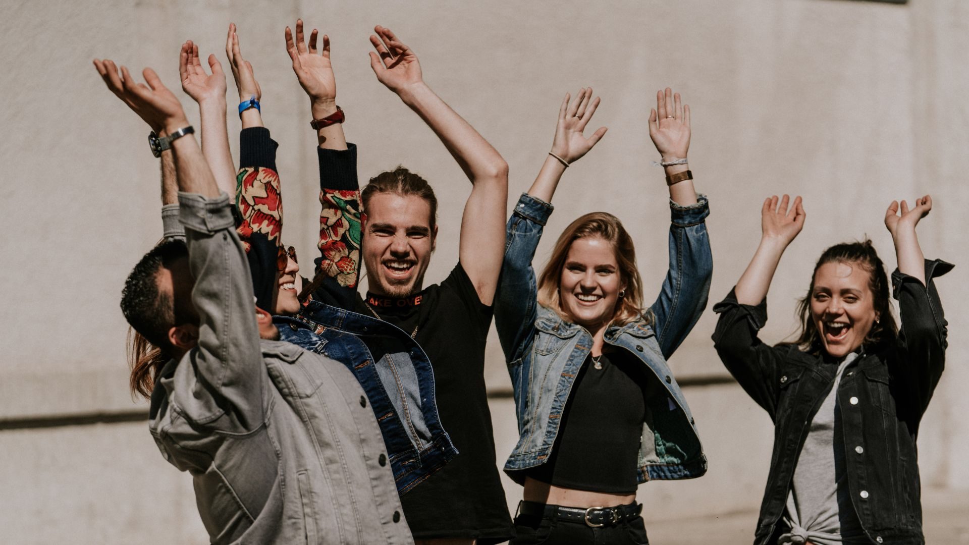 Menschen lachen, freuen sich und feiern zusammen im Freien vor einer Gedenkwand.